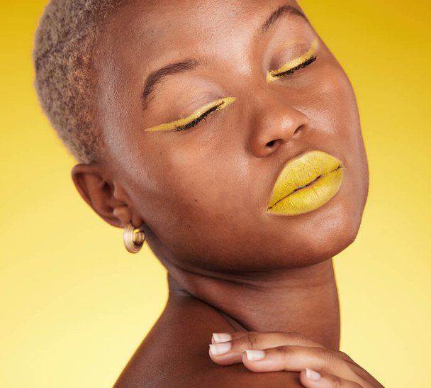 Kosmetik, Kunst und Frau in einem Studio mit Make-up-Eyeliner und Lippenstift für die Kosmetik. Schönheit, kreatives und junges afrikanisches Model mit buntem Glamour-Gesicht vor gelbem Hintergrund - Foto, Bild