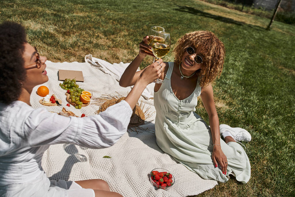 africké americké ženy cinkající sklenice na víno při relaxaci na letním pikniku v parku, banner - Fotografie, Obrázek