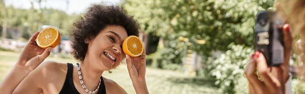 Unbekümmerte Afroamerikanerin amüsiert sich mit Orangenhälften im Sommerpark, Banner - Foto, Bild