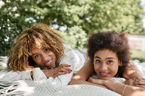young african american girlfriends laying on blanket in park and smiling at camera, summer leisure - Photo, Image