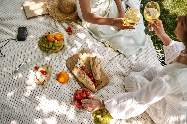 vista superior, piquenique, namoradas americanas africanas com copos de vinho perto de frutas, legumes, pão - Foto, Imagem
