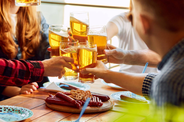Young people, friends meeting together on warm day, sitting in pub, drinking delicious lager beer and having pleasant time together. Concept of oktoberfest, traditional taste, leisure time, enjoyment - Photo, image