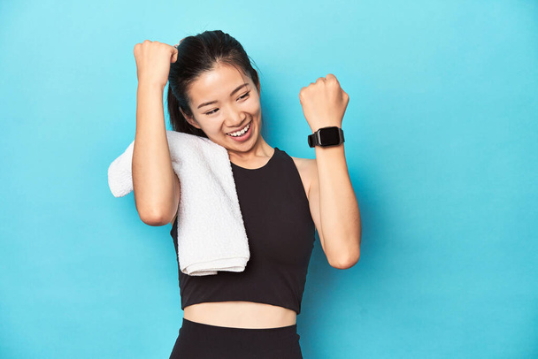 Atleta asiático enérgico celebrando, con smartwatch y toalla. - Foto, imagen