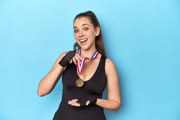 Αθλητική γυναίκα με χρυσό μετάλλιο σε μπλε φόντο στούντιο. - Φωτογραφία, εικόνα
