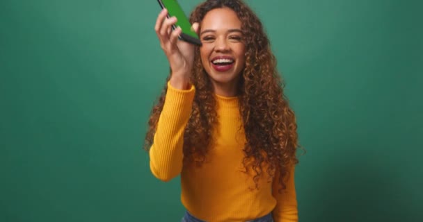 Heureuse jeune femme tient l'écran de clé chromatique de dispositif, fond de studio vert. Images 4k de haute qualité - Séquence, vidéo