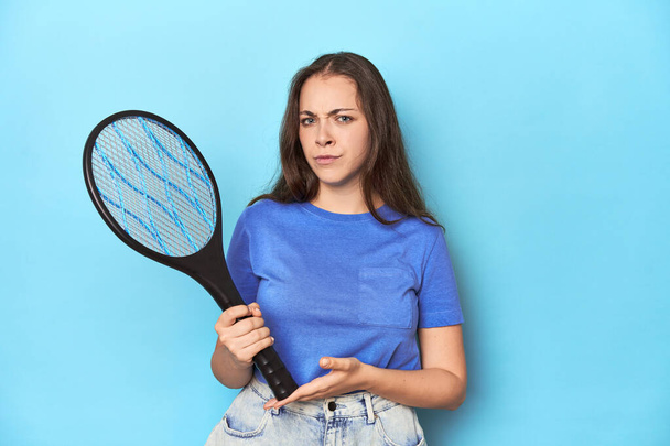 Γυναίκα που κρατάει ένα ηλεκτρικό κουνούπι σε ένα μπλε στούντιο. - Φωτογραφία, εικόνα