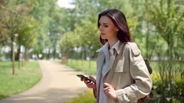 Heureuse femme d'âge moyen tapez quelque chose dans le smartphone tout en attendant son petit ami dans le parc de la ville sur un rendez-vous. Se sont heureux, penser à quelque chose et flirter. Concept de relation entre un homme et un - Séquence, vidéo