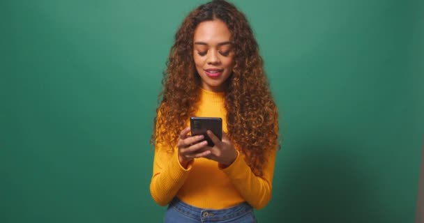 Mujer birracial joven lee mensaje de texto conmocionado emocionado, fondo de estudio verde. Imágenes de alta calidad 4k - Imágenes, Vídeo