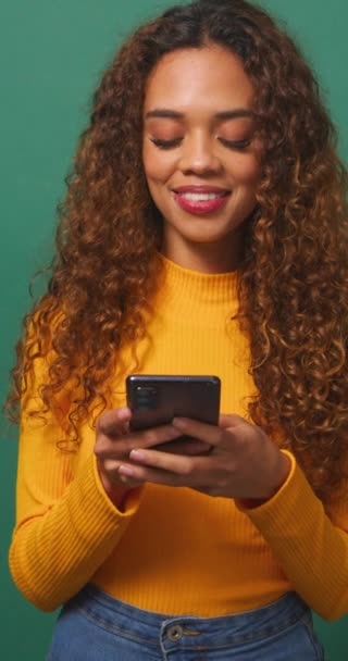 Schöne junge Frau, SMS auf dem Handy, lächelnd, grüner Studiohintergrund. Hochwertiges 4k Filmmaterial - Filmmaterial, Video