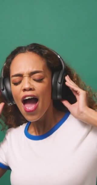 Young biracial woman dancing with headphones, green studio background. High quality 4k footage - Footage, Video