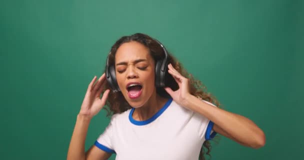 Junge Frau tanzt mit Kopfhörern, grüner Studiohintergrund. Hochwertiges 4k Filmmaterial - Filmmaterial, Video
