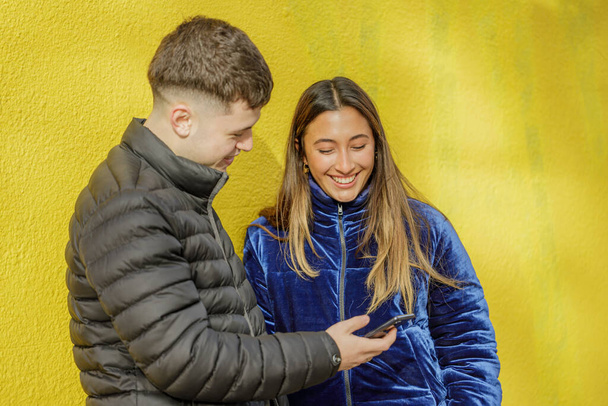 Латинська дівчина посміхається з кавказьким хлопчиком на жовтому фоні. - Фото, зображення