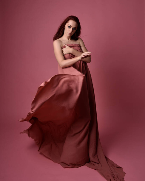  Portait de mulher bonita vestindo vestido de tecido de seda drapeado, em pé pose. Isolado no fundo do estúdio rosa. - Foto, Imagem
