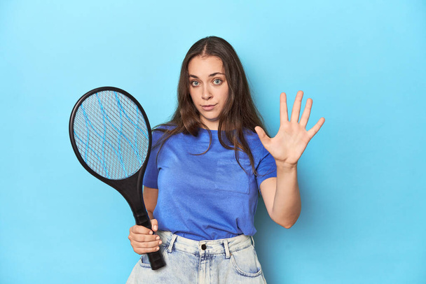 Nő egy elektromos bug zapper a kék háttér mosolygós vidám mutatja az ötös számú ujjaival. - Fotó, kép