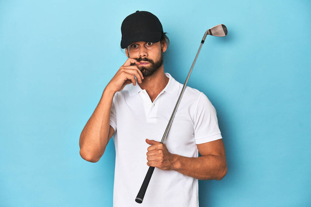 Μακρυμάλλης παίχτης του γκολφ με ρόπαλο και καπέλο που δαγκώνει νύχια, νευρικός και πολύ ανήσυχος. - Φωτογραφία, εικόνα