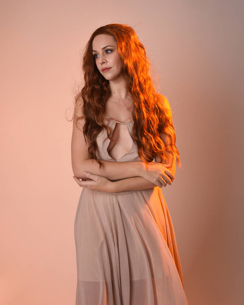 Κοντινό πορτρέτο του όμορφου μελαχρινού γυναικείου μοντέλου φορώντας ένα κρεμ φόρεμα με χρυσαφί φως στην πλάτη.Το χέρι της χειρονομίας ποζάρει με τα χέρια απλωμένα, απομονωμένα στο φόντο του στούντιο. - Φωτογραφία, εικόνα