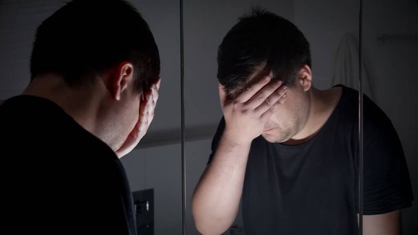 Triste homem frustrado olhando no espelho e suspirando. Conceito de depressão, suicídio, estresse, doença mental, solidão e frustração. - Foto, Imagem