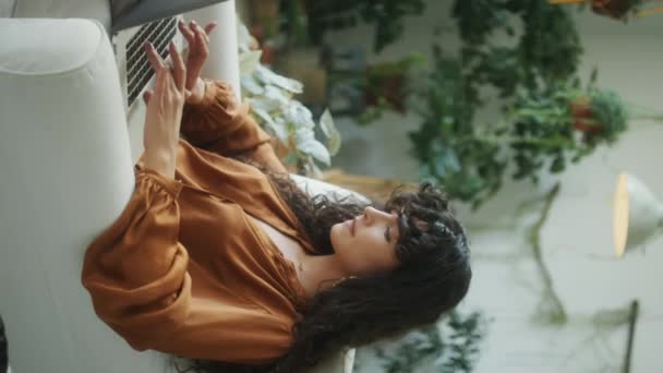 Függőleges felvétel fiatal nő dolgozik laptop, miközben ül a karosszékben a szobában a városi dzsungel belső - Felvétel, videó