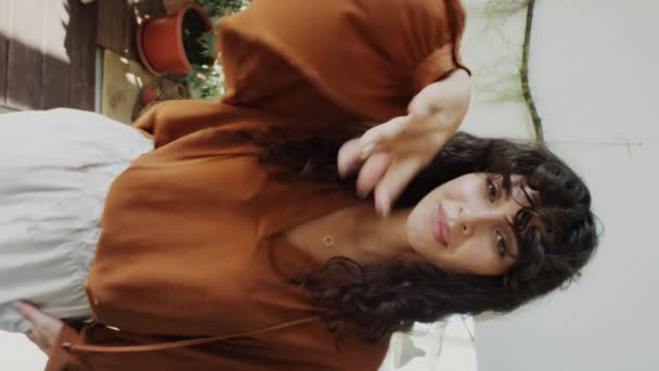 Вертикальний знімок привабливого жіночого впливу знімає руку з камери і посміхається, позуючи в стильному вбранні для модного блогу - Кадри, відео