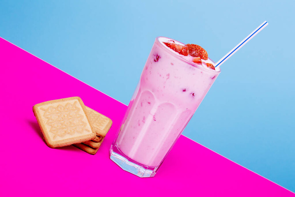Glas Erdbeerjoghurt mit Keksen auf buntem Hintergrund. Erdbeerjoghurt auf blauem und rosa Hintergrund. Glas Erdbeerjoghurt bedeckt von frischen Erdbeerscheiben.  - Foto, Bild