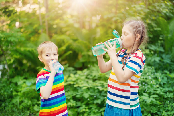 Des enfants avec des bouteilles d'eau dans les mains debout à l'extérieur et buvant. Soif après avoir marché. - Photo, image