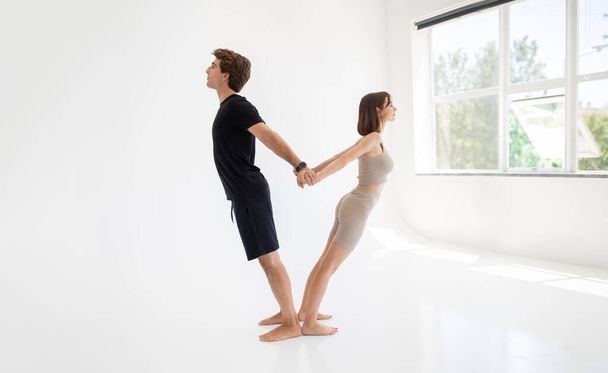 Happy calm young caucasian lady and guy in sportswear enjoy workout together, stretching body, meditate, practice yoga in gym or room interior. Teamwork, sports at home, health care - Photo, image