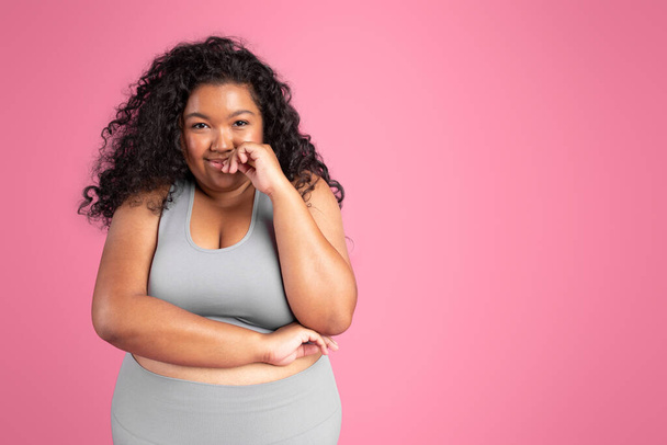Retrato de atraente jovem preto plus tamanho mulher em sportswear olhando e sorrindo para a câmera, posando no fundo do estúdio rosa, espaço livre - Foto, Imagem