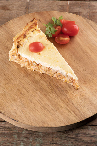 ломтик куриного пирога с сыром и помидорами черри на круглой деревянной доске на деревенском столе под углом зрения крупным планом с петрушкой - Фото, изображение