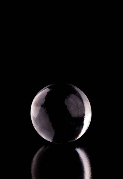 hielo translúcido cristalino y esfera de cristal aislados sobre fondo negro con reflexión desde el frente - Foto, Imagen