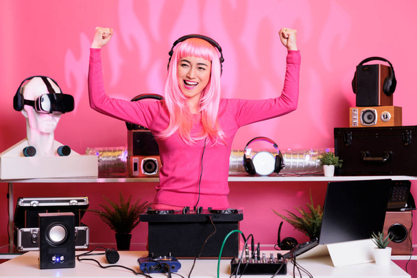 Performer with pink hair performing techno music using dj mixer console enjoying to play song with fans, having fun in club at night. Artist doing performance with professional audio equipment - Foto, Imagem
