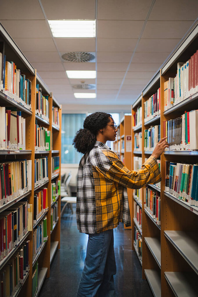 Een studente die een boek kiest om te lezen voor een examen. Ze is in een bibliotheek.. - Foto, afbeelding