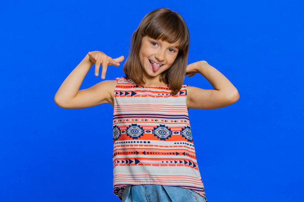 Cheerful funny bully young cute girl showing tongue making faces at camera, fooling around, joking, aping with silly face, teasing. Preteen brunette child kid on blue background. Little children - Photo, Image