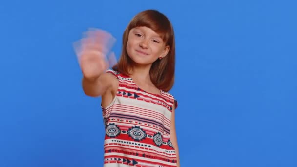 Jong schattig brunette schoolmeisje glimlachend vriendelijk op camera en zwaaiende handen gebaren hallo of vaarwel, gastvrij met gastvrije uitdrukking. peuter vrouw kind kind geïsoleerd op blauwe achtergrond - Video
