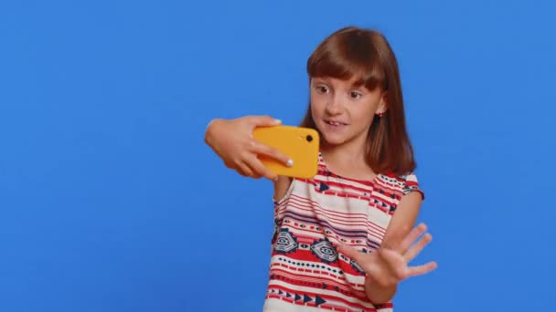 Mladá školačka blogger vliv brát selfie na smartphone, komunikovat videohovor on-line s odběrateli v aplikaci sociálních médií. Preteen kavkazské dítě dítě izolované na modrém pozadí studia - Záběry, video