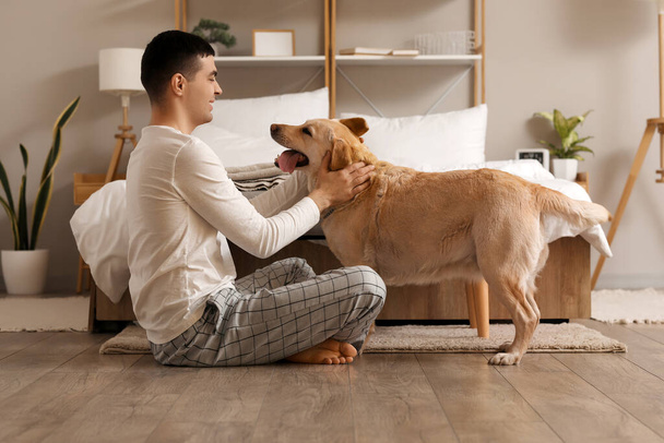 Young man with cute Labrador dog in bedroom - Fotó, kép