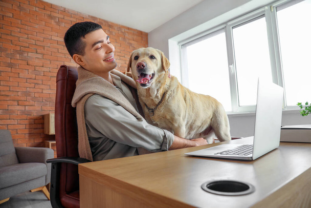 Young man with cute Labrador dog at table in office - Photo, Image