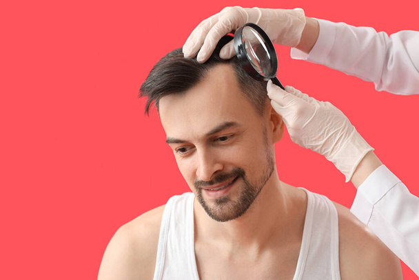 Docteur examinant les cheveux du jeune homme avec loupe sur fond rouge, gros plan - Photo, image