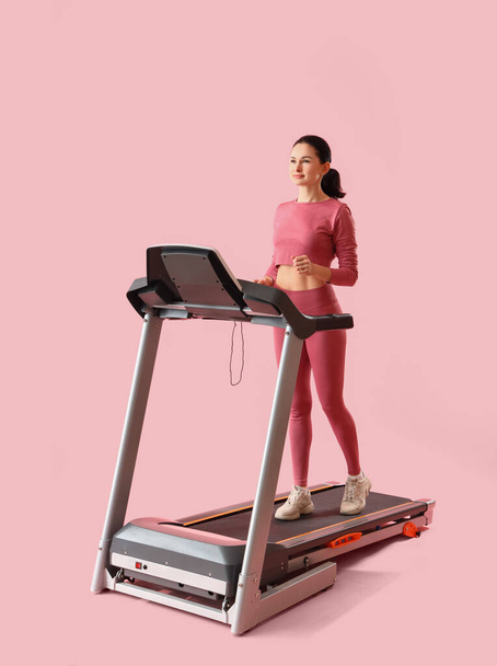 Schöne Frau trainiert auf Laufband vor rosa Hintergrund - Foto, Bild