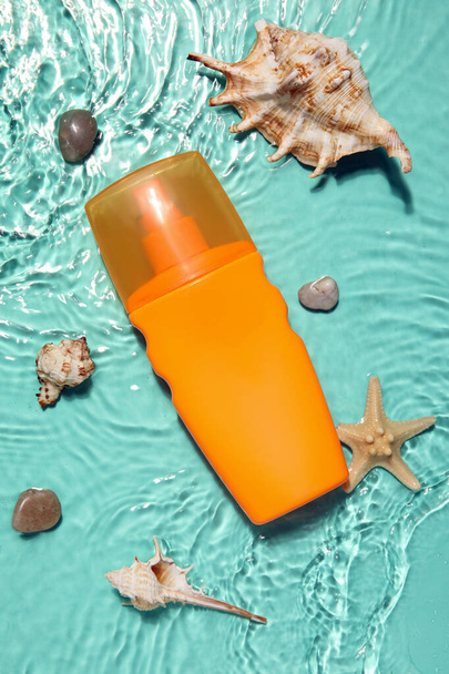 Sunscreen cream with starfishes and seashells in water on color background - Fotó, kép