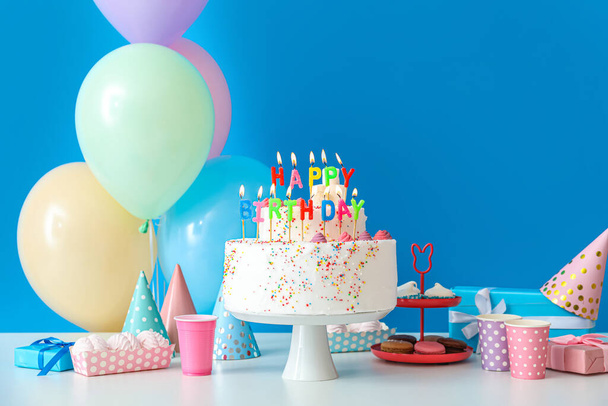 Τούρτα γενεθλίων με διάφορα γλυκά στο τραπέζι κοντά στο μπλε τοίχο - Φωτογραφία, εικόνα