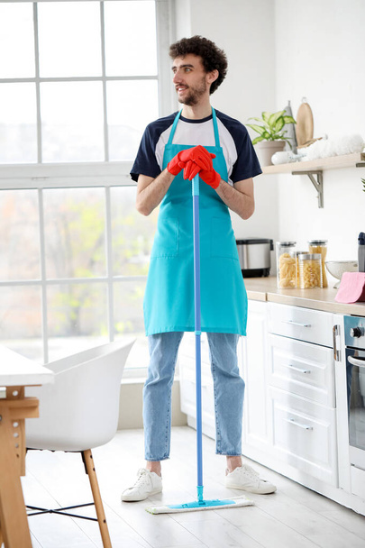 Молодий чоловік маскує підлогу на кухні
 - Фото, зображення
