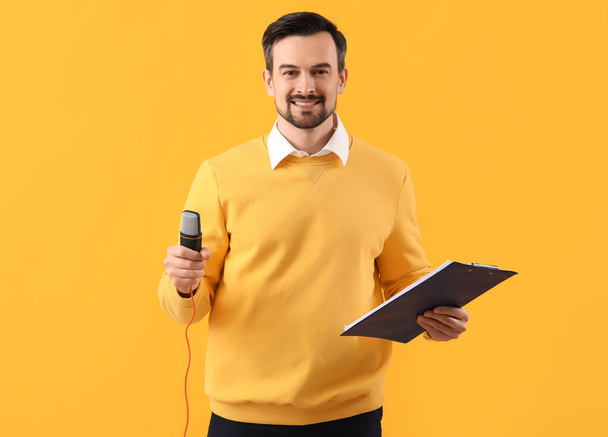 Male journalist with microphone and clipboard on yellow background - Φωτογραφία, εικόνα