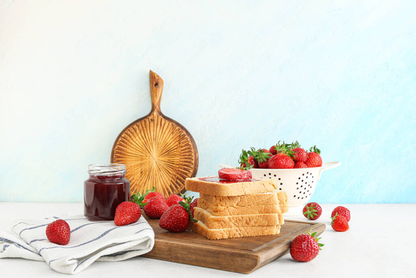 Fa tábla ízletes pirítóssal, édes eper lekvárral és friss bogyókkal az asztalon - Fotó, kép