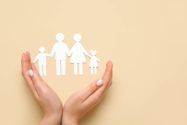 Жіночі руки з фігурами сім'ї на бежевому фоні. Концепція страхування - Фото, зображення