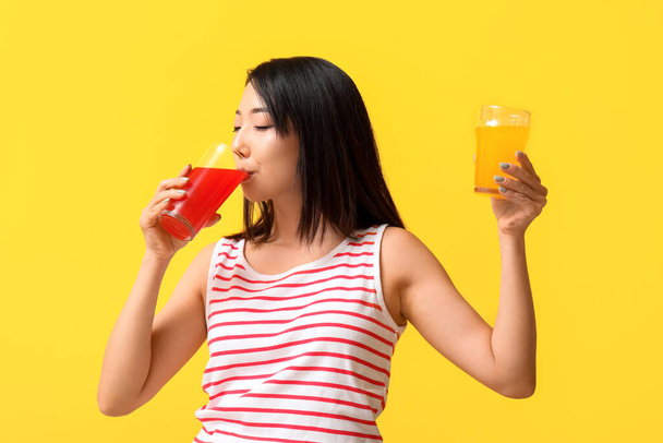 Beautiful Asian woman with glasses of juice on yellow background - Foto, Bild
