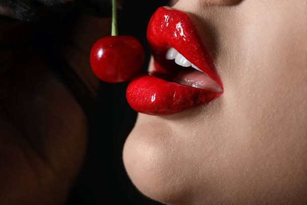 Beautiful woman with red lips and cherry on dark background, closeup - Photo, image