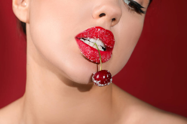 Beautiful woman with sugar lips and cherry on red background, closeup - Photo, Image