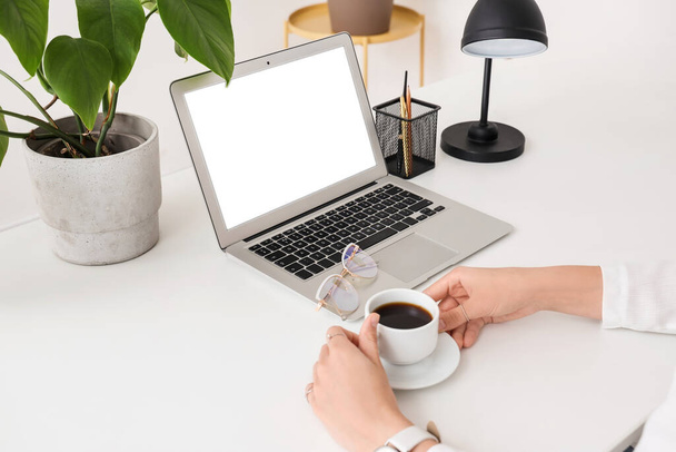 Kobiece ręce z filiżanką kawy i laptopem przy białym stole - Zdjęcie, obraz