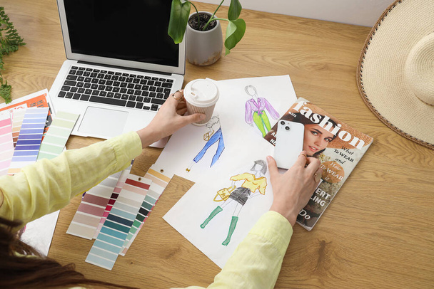 Diseñador de moda trabajando en la mesa con teléfono móvil, taza de café, muestras de color y portátil - Foto, Imagen