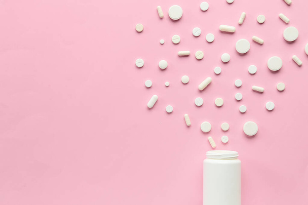 Verschiedene Pillen, die aus der Tablettenflasche auf rosa Hintergrund austreten - Foto, Bild